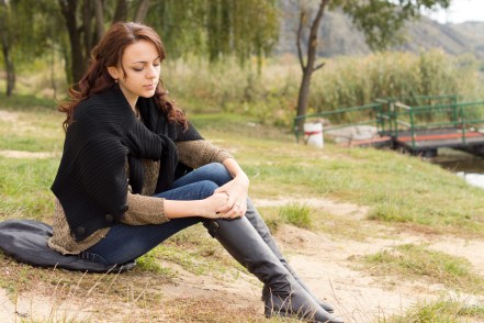 Lonely young woman sitting holding her knees, looking down