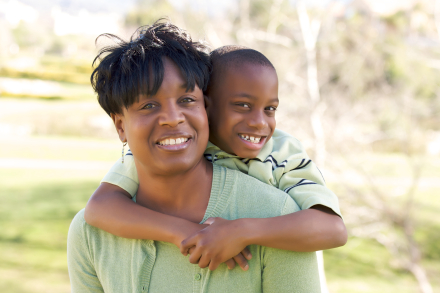 Happy mom with young son hugging her shoulders from behing