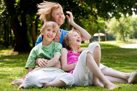 Two children laughing with mom on ground