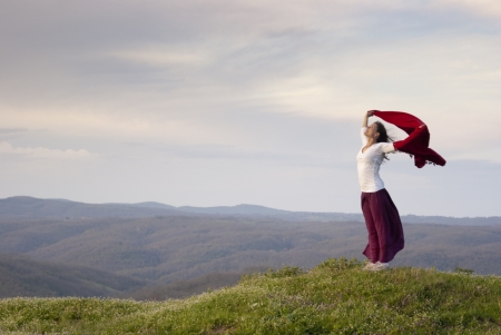 Woman standing on top of hill, arms spread holding a cape in the wind