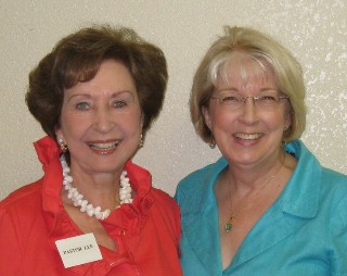 Two smiling women standing together, one wearing a bright red top and the other in a turquoise blouse.