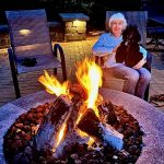 Gail seated with poodle in her lap in front of an outdoor fire pit
