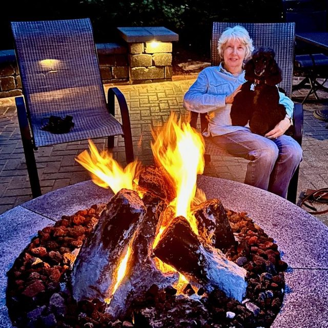 Gail seated with poodle in her lap in front of an outdoor fire pit